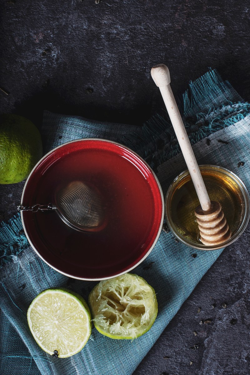 tea steeping in a red mug with lemons and honey on a blue towel and black table, herbal tea 4k