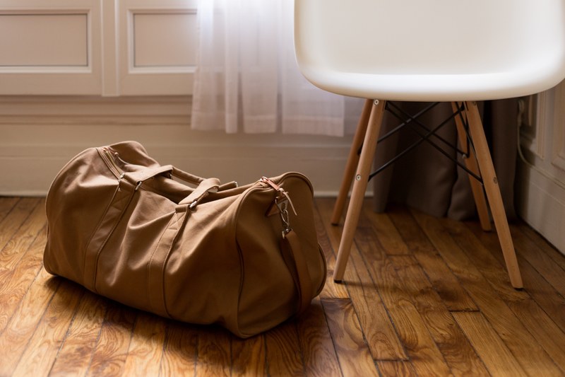 a leather duffel bag on the floor next to a small white chair, leather duffel bag 4k
