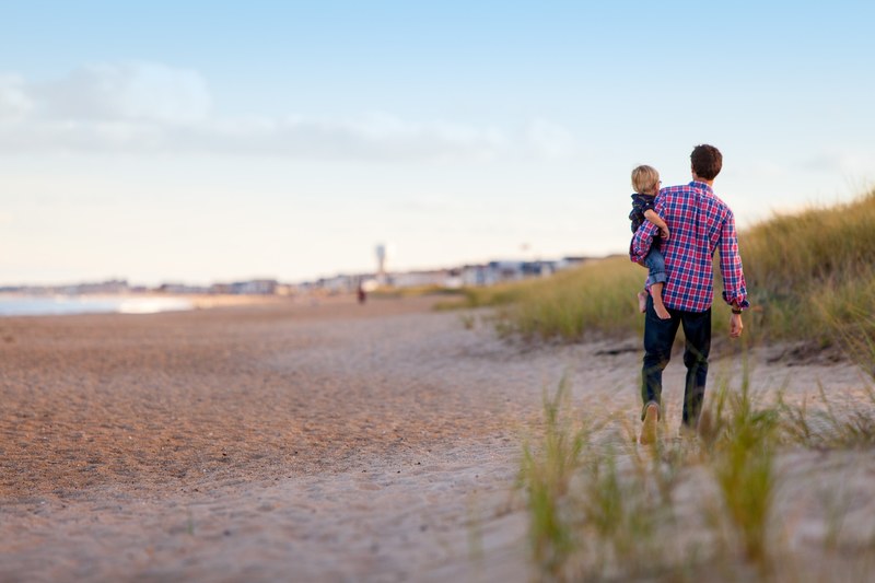 father in plaid shirt and jeans holds child on hip as they walk along the dunes, among the dunes 4k