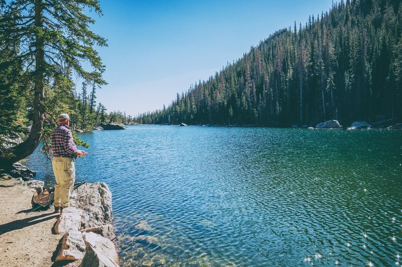 a man with a fishing pole on the shore of emerald lake, fisherman over a lake 4k
