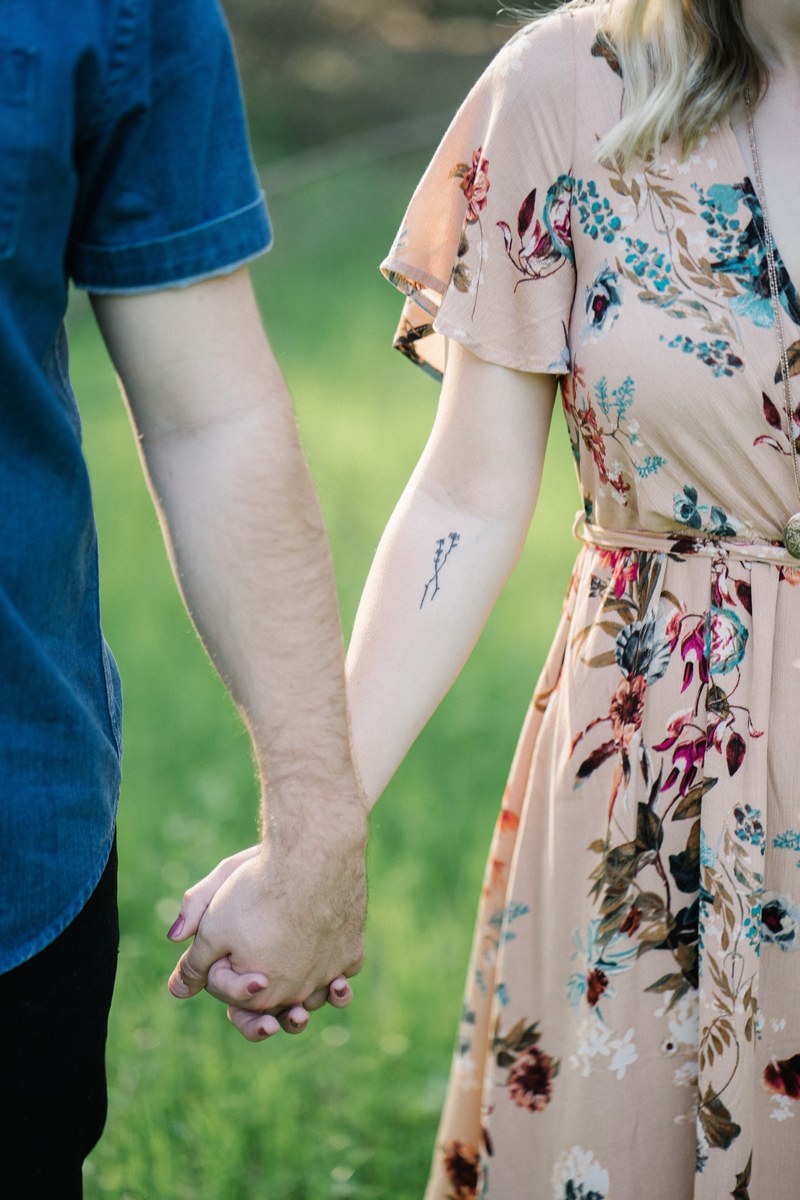 a man and a woman standing outdoors hold hands she has a tattoo on her arm, _holding hands in a meadow 4k