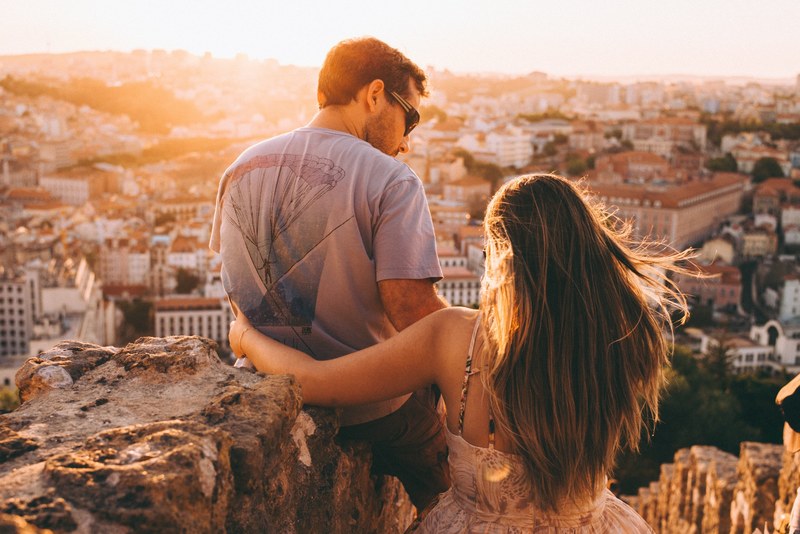 a couple sits together against rocks overlooking lisbon in the sunshine, lisbon in the sunshine 4k