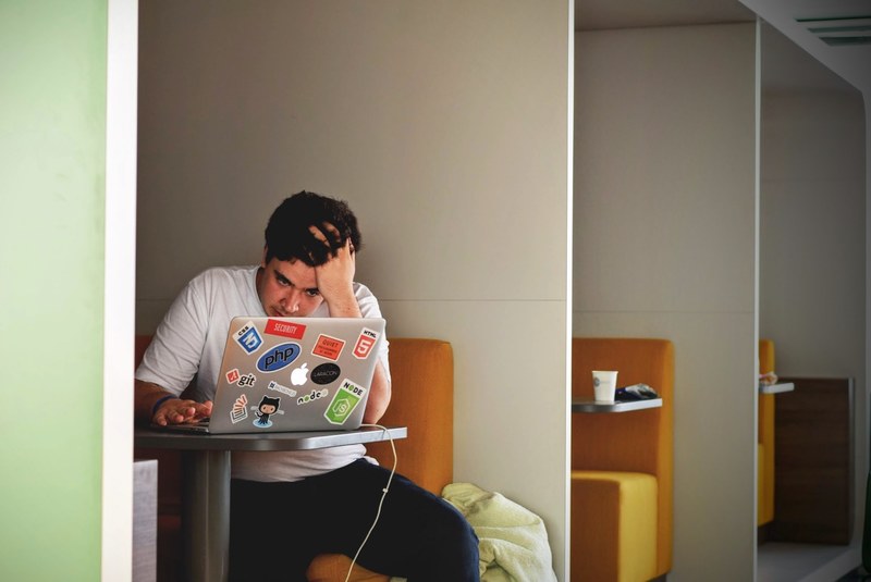 a focused man working on a sticker covered laptop in a coffee shop, full focus at a coffee shop 4k