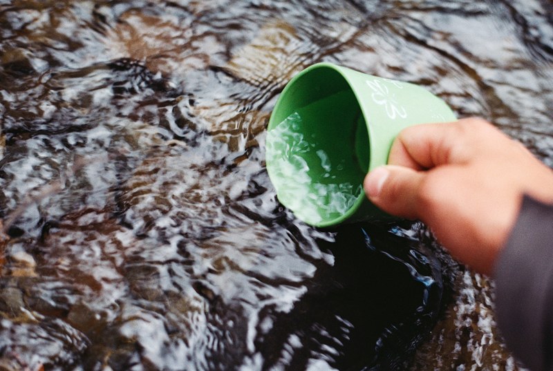 a person filling up a green mug in a river in torres del paine national park, torres del paine national park 4k