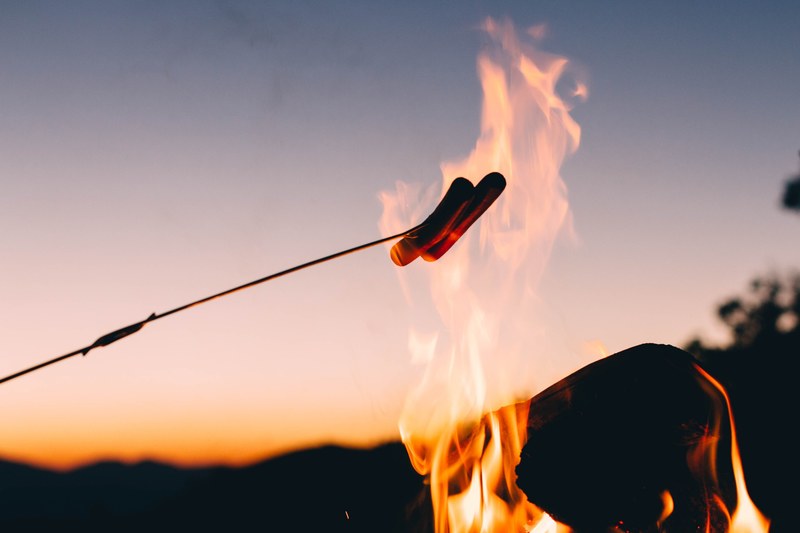 roasting hotdogs over an open campfire at night, campfire cooking 4k