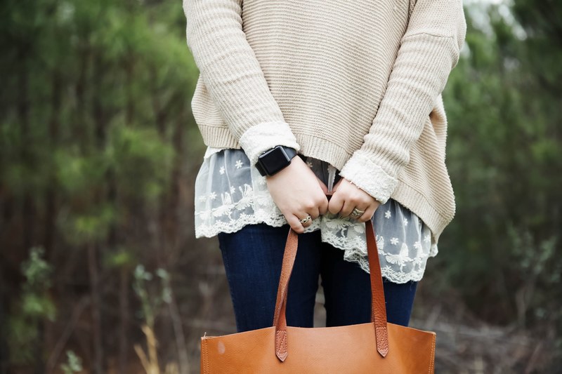 a woman wearing a sweater and an apple watch holding a leather bag in suwanee, holding on 4k
