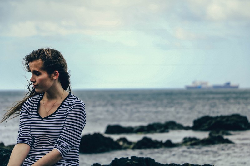 wind blows a womans hair as she stands on the sea shore, alone by the ocean 4k
