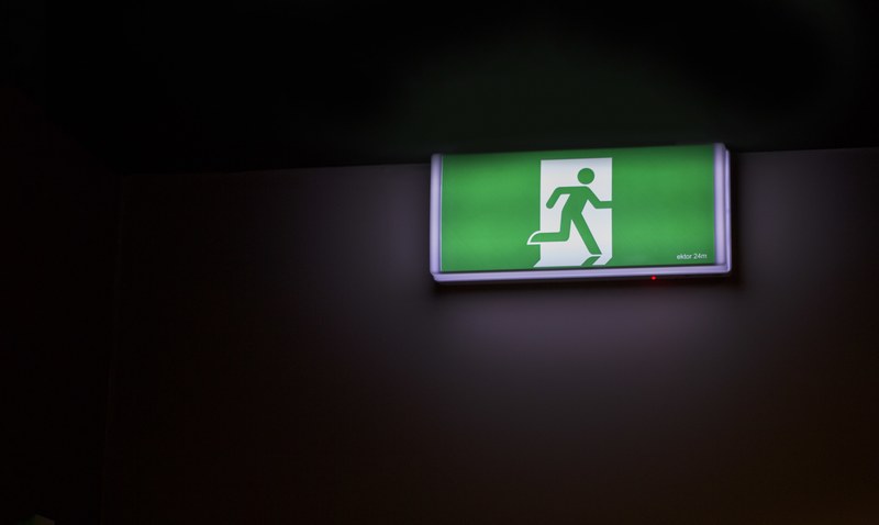 green exit sign with figure of a person exiting through a door against a black background, exit 4k