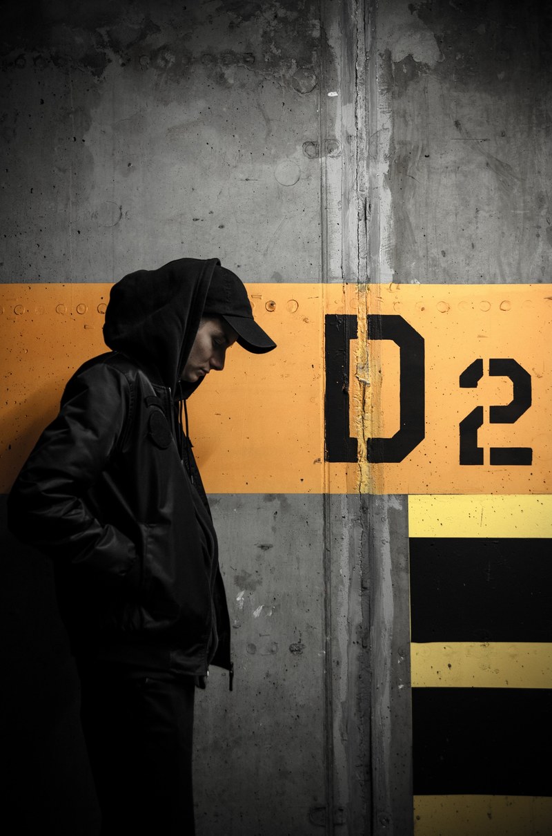 man with hoodie and cap standing next to a concrete wall, man by a concrete wall 4k
