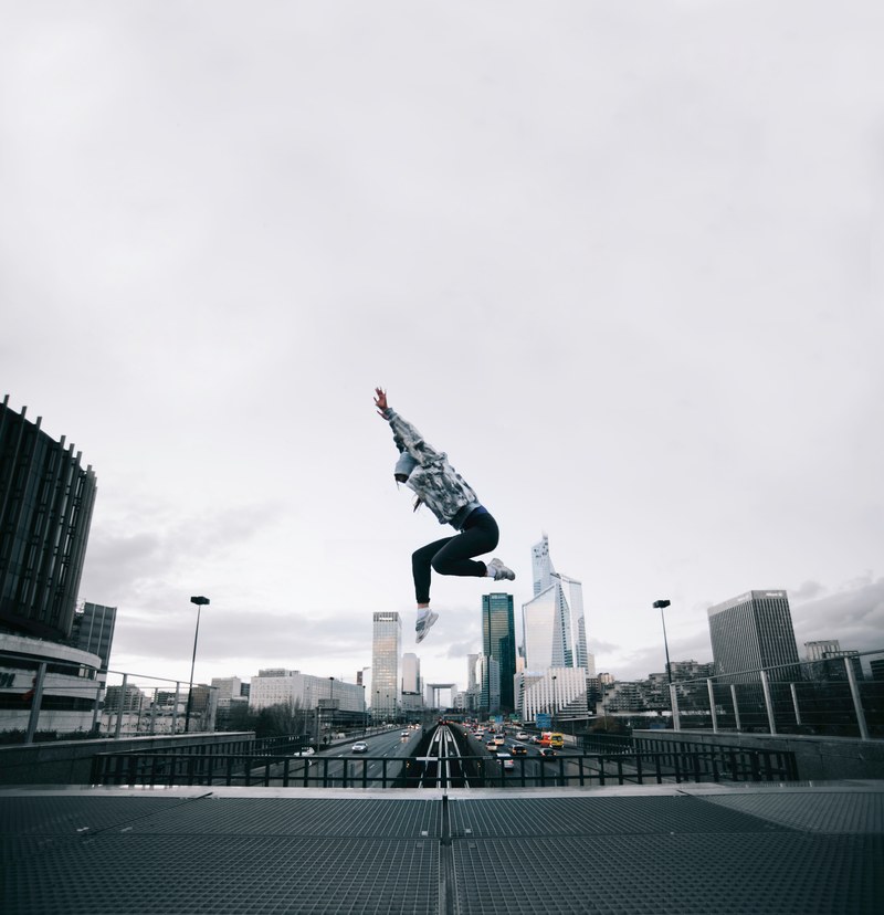 a woman jumping in front of an urban backdrop of buildings and roads, end of the line_ 4k