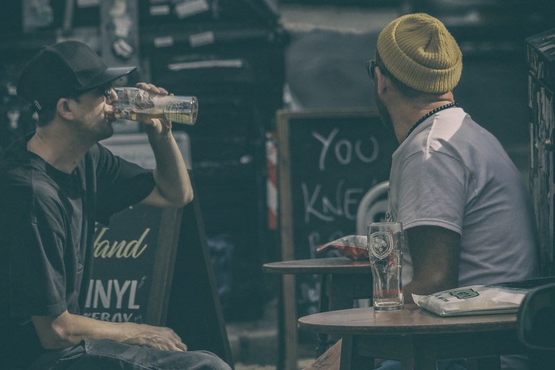 two men both wearing hats t shirts and glasses and drinking beer in brighton, two men both wearing hats 4k