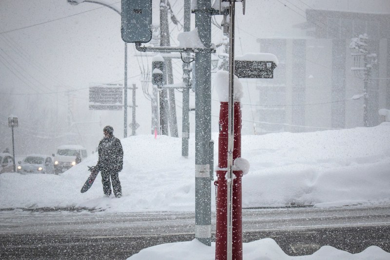 a snowboarder carrying his board and waiting to cross the street in hirafu japan, snowfall in hirafu 4k