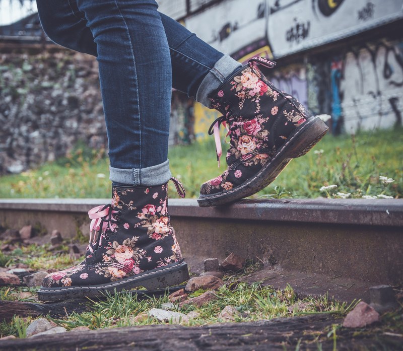 a close up shot of a person wearing floral boots stepping on a railway track with graffiti behind, floral boots and graffiti 4k