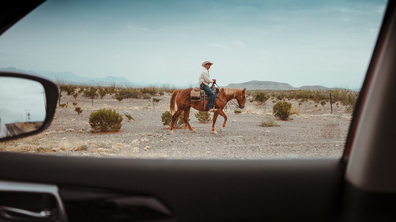 looking out the car window at a cowboy riding a horse in the desert, rider on the storm 4k
