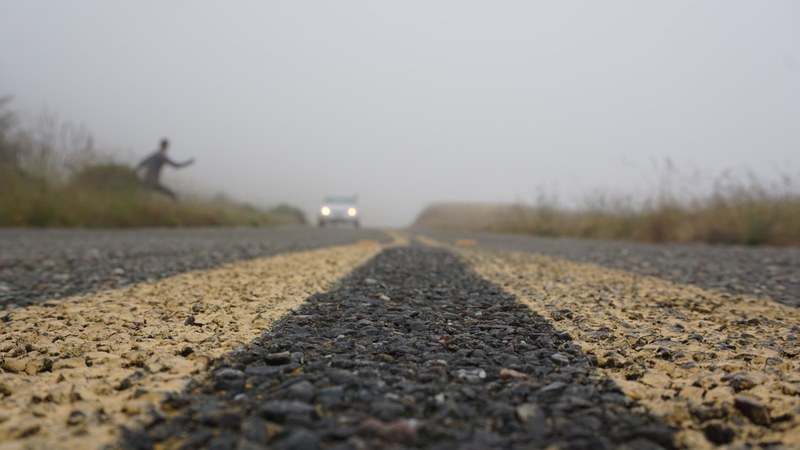 road level view of a person crossing the foggy road, _hitchhiking in the country 4k