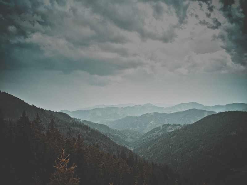 a mountainous landscape in fog under heavy clouds, turquoise haze over mountains 4k