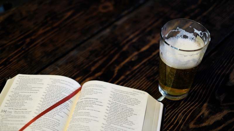 a large hardcover book next to a glass of beer, _bible beer 4k