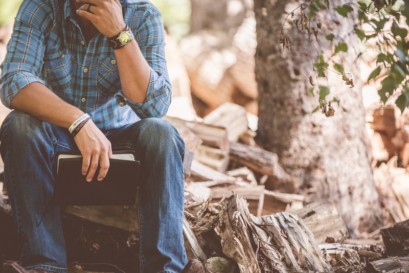 a thoughtful man with a notebook sitting on a pile of firewood, lost in thoughts 4k