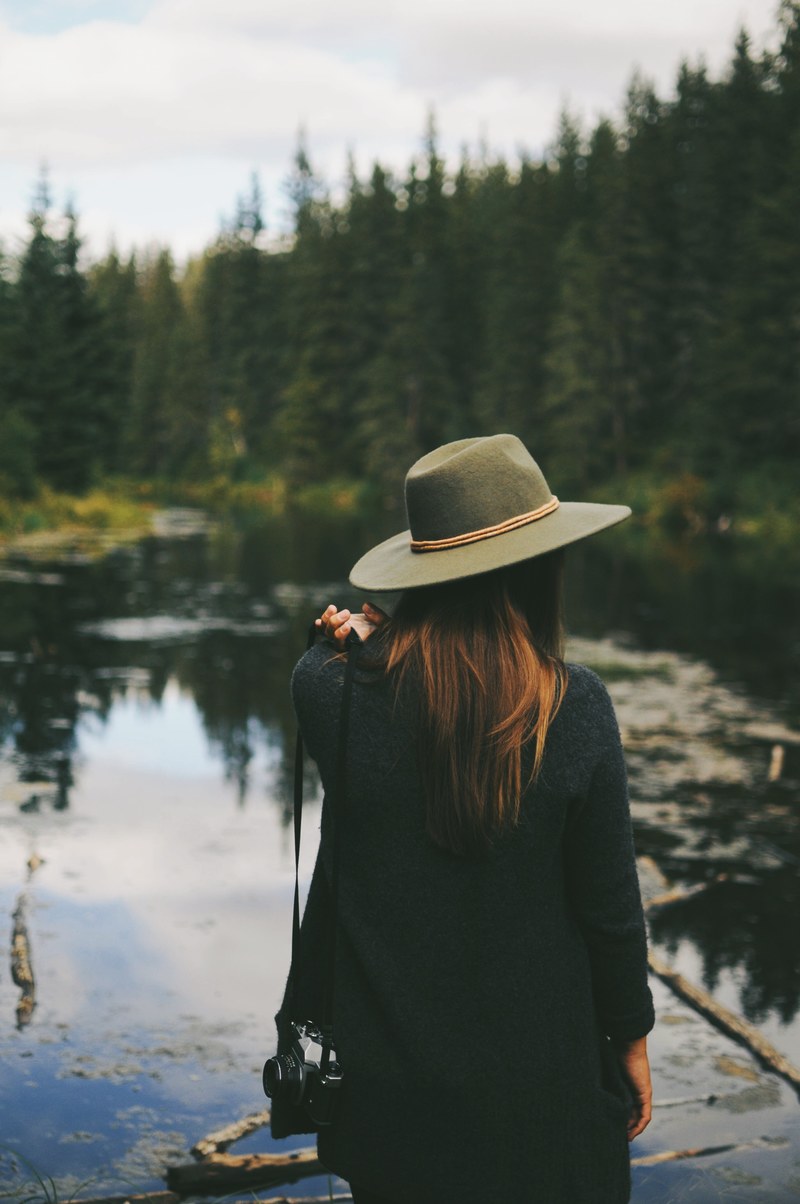 a woman wearing a hat staring out at the lake at mactaggart sanctuary near edmonton, view of a lake near edmonton 4k