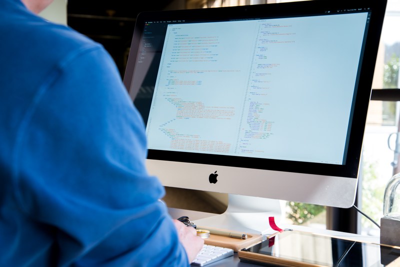 a person working at an imac with lines of code on its screen, developer working on an imac 4k