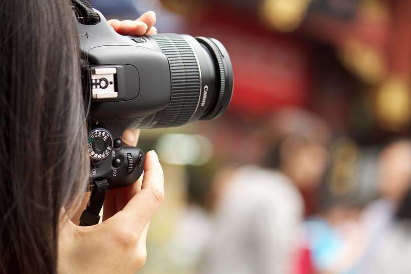 a woman with brown hair tilting a canon dslr camera vertically to take a picture of a red and orange blurred background, photographer with canon camera 4k