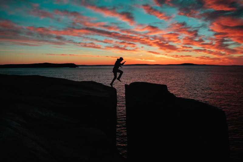a man leaping between large rocks near the ocean, leap of faith 4k