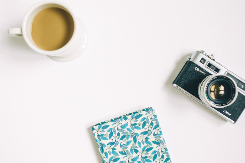 a flatlay of a latte a floral coaster and a vintage camera on a white surface, camera coaster and coffee in flatlay 4k
