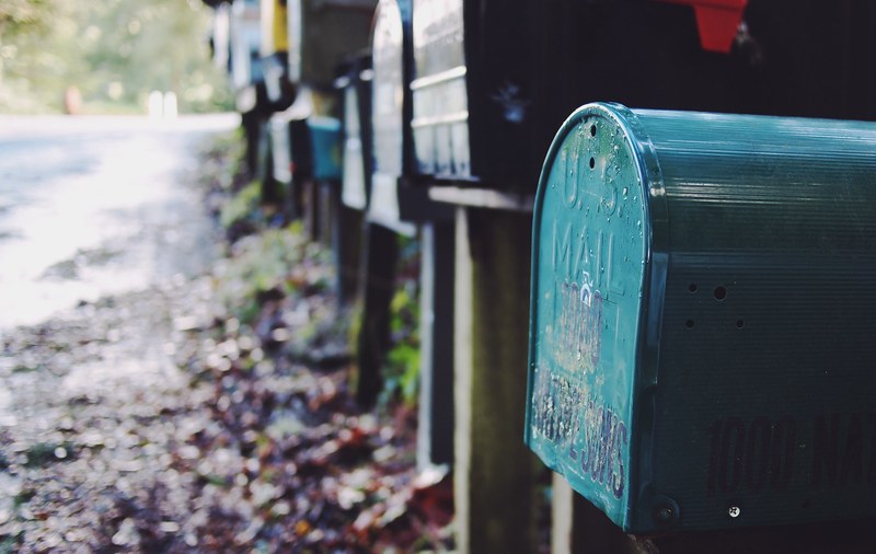 multiple multicolored mailboxes placed alongside a muddy street strewn with leaves, macro mailbox 4k