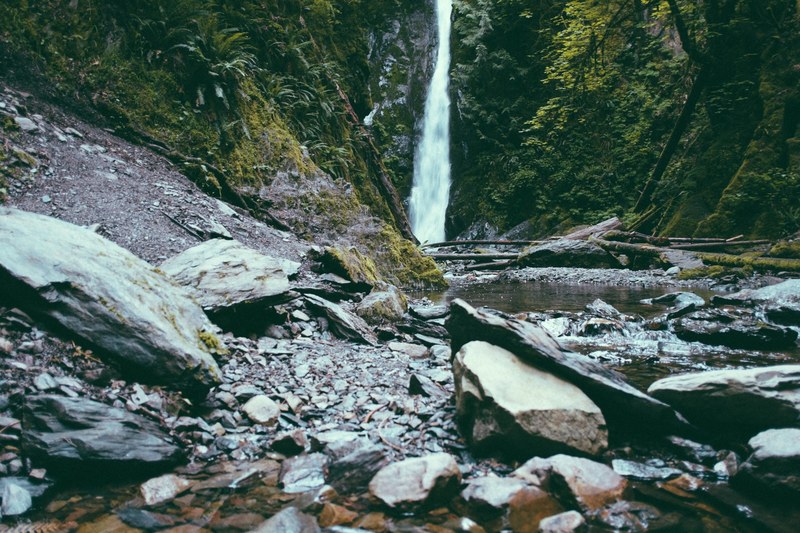 a waterfall pouring down into a rocky creek in a forested area, rocky creek with a waterfall 4k