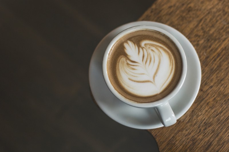 latte with foam leaf like art in a white coffee cup on a wooden table, latte artwork cincinnati 4k
