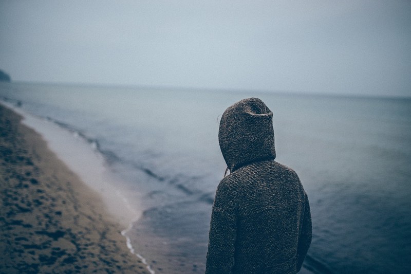 person in a hoodie on a sandy beach filled with footprints, person in a hoodie 4k