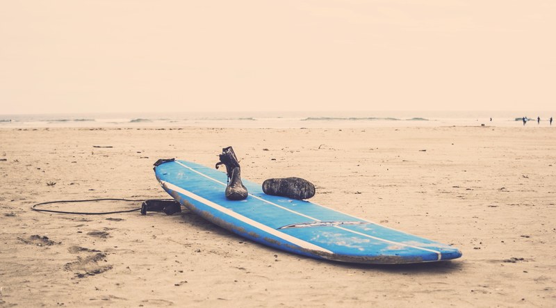 boots on a dirty blue surfboard on the sand beach, abandoned surfboard 4k