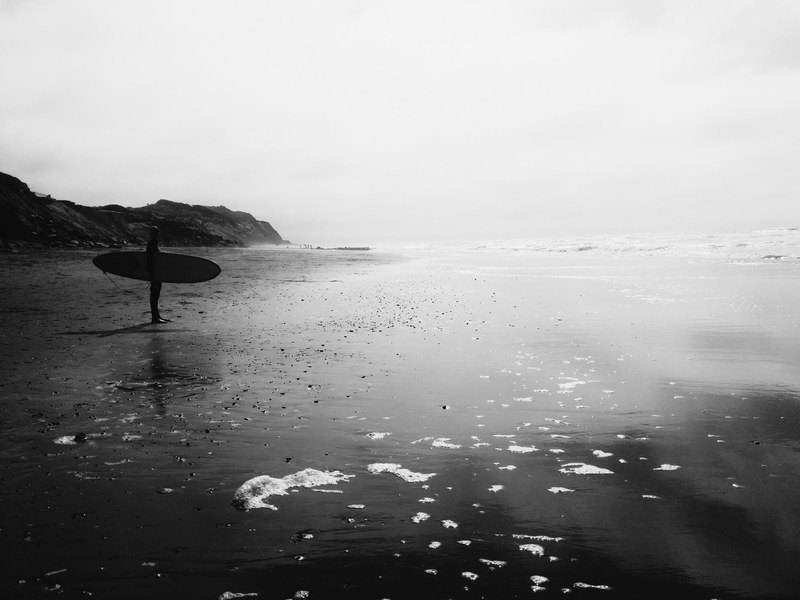 a person holding a surfboard on the beach looking out to the ocean, surfer looking for the waves 4k