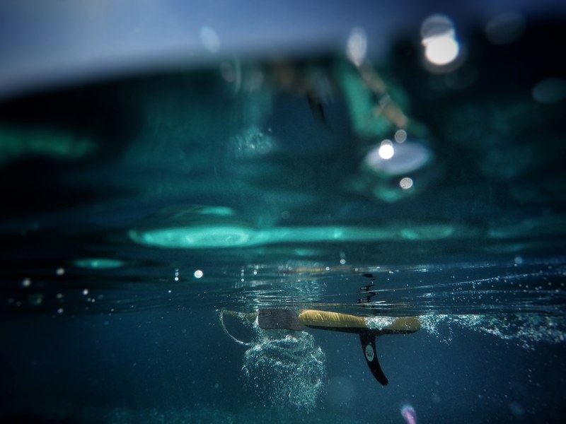 an underwater shot of a surfboards fin in the blue mediterranean sea, under the surfboard 4k