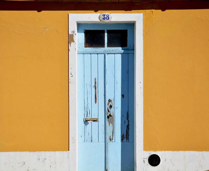 old wooden door with chipped blue paint with a brass doorknob and the number 38 at the top surrounded by mustard yellow walls, baby blue door and yellow walls 4k