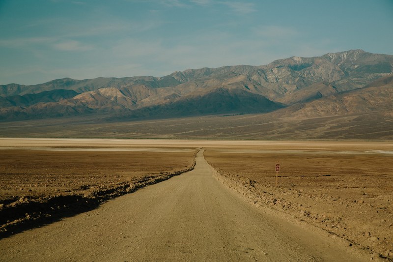 a long dirt road leading towards the rocky mountains in an arid environment, dry dirt road 4k