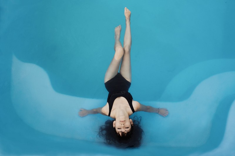 a brunette woman wearing a black bathing suit floating in a swimming pool, floating in a pool 4k