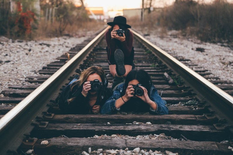 three young women with cameras taking a photo while on a railroad track, pictures on a railroad track 4k
