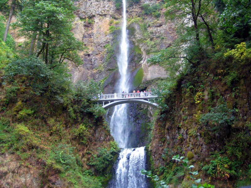people standing on a white bridge over a waterfall pouring down from a rocky face, people on a white bridge over a waterfall 4k