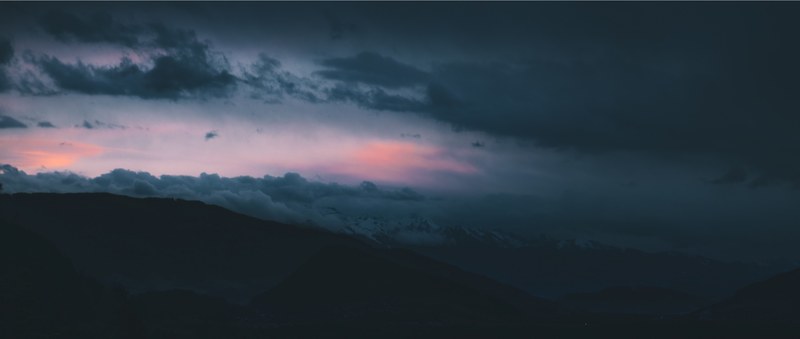 dark clouds roll over silhouettes of hills at sunset, cloudscape at night 4k