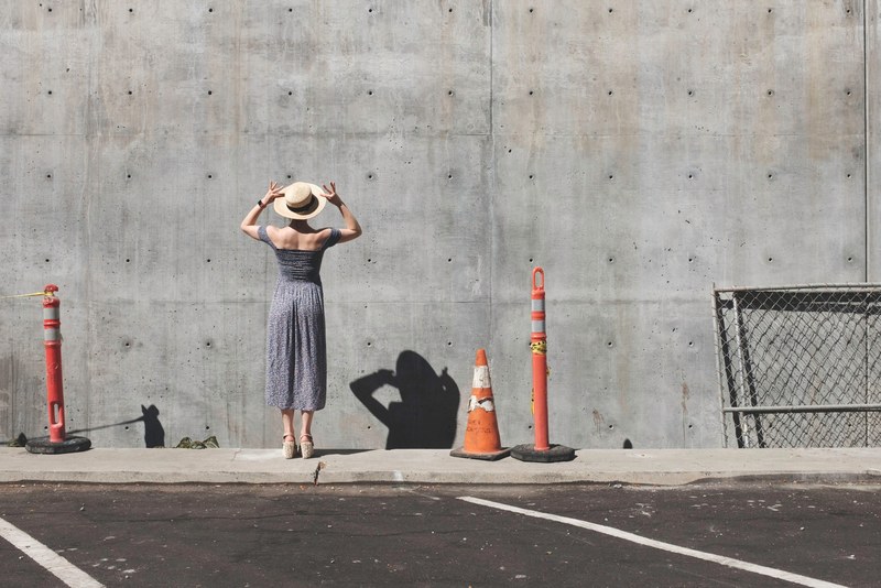 a woman in a dress and a hat standing near traffic cones by a concrete wall, woman in a dress by a wall 4k