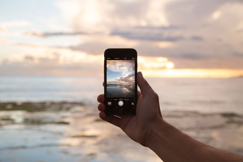 a hand holding out an iphone for a landscape picture of the evening sky and the setting sun, hand holding iphone with a setting sun 4k
