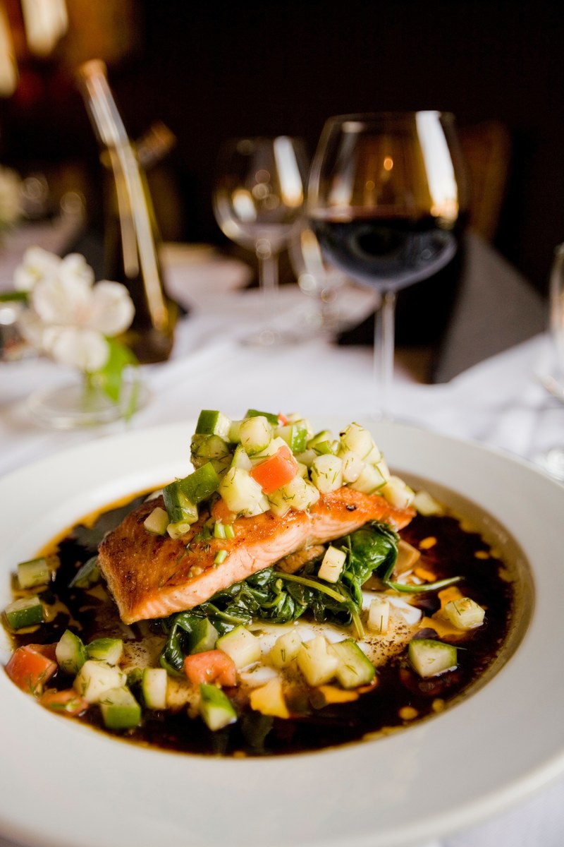 a deep dish with a meal with salmon and zucchini next to a wine glass on a white tablecloth, meal with salmon and zucchini 4k