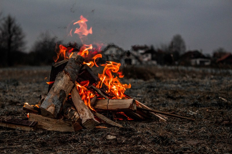 a pile of logs burning in a dead field beside a rural village in the fall or winter, exploring and camping with friends 4k