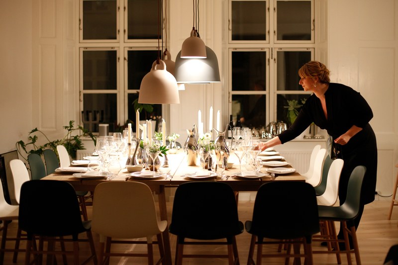 a woman setting a table and lighting candles for a dinner party in her living room in copenhagen, velbekomme 4k