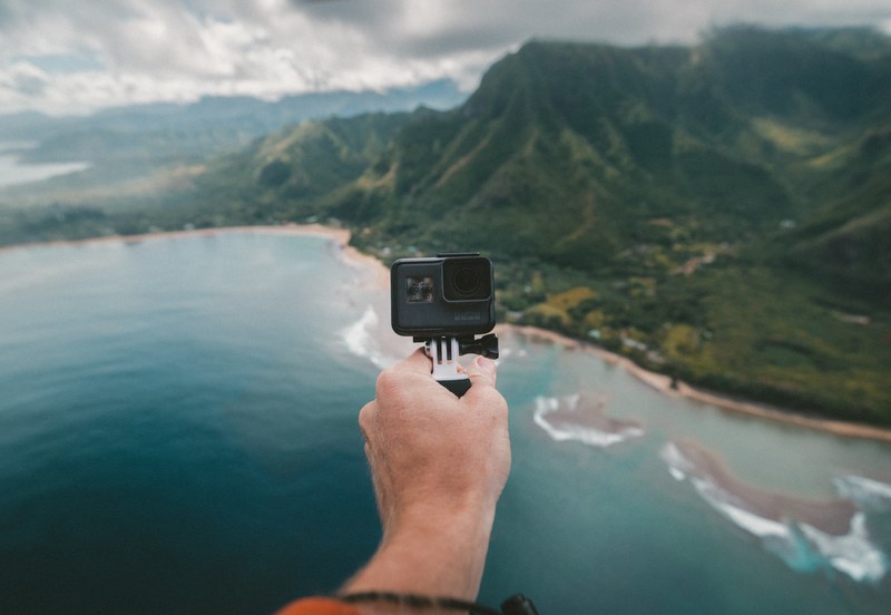a person pointing a gopro camera at themselves while standing high above the coast, ariel gopro 4k