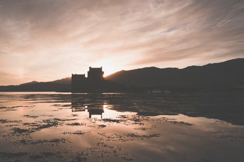 a silhouette of a castle at the shore of a lake at sunset, eilean donan castle 4k