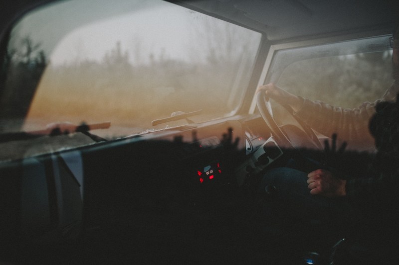 looking into dashboard of car with driver and steering wheel window reflects trees, frenham 4k