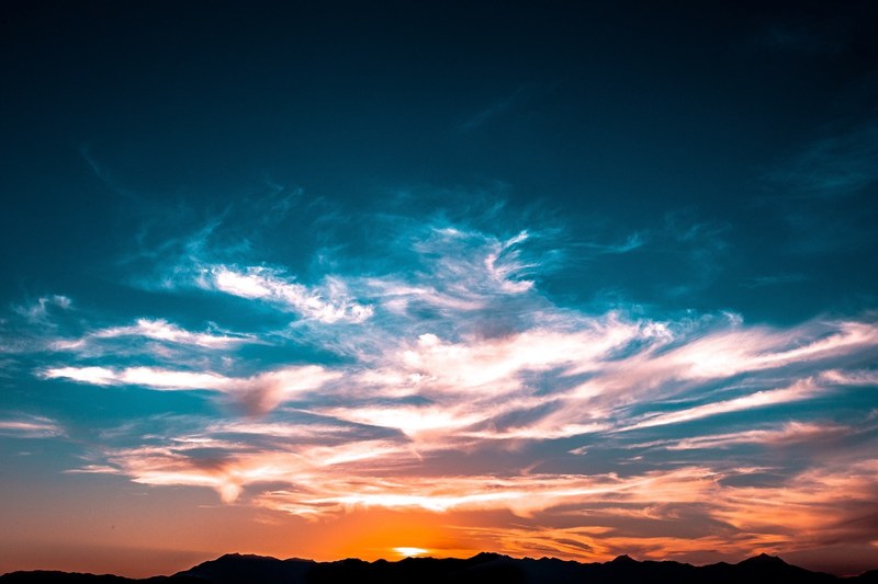 wispy clouds against the illuminated orange and blue sky with the sun behind the hills, _clouds orange blue sky 4k
