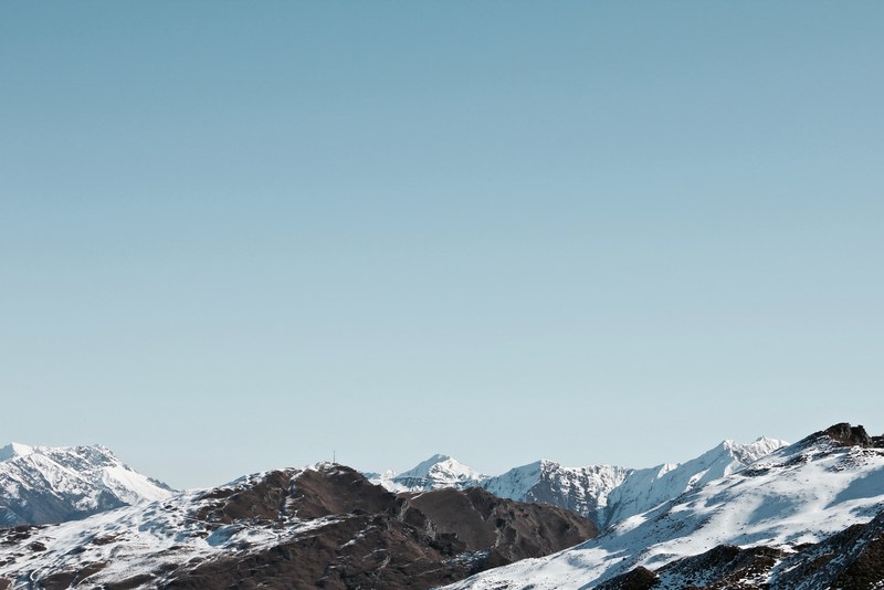 a mountain range dusted with snow under a pale blue sky, snow dusted mountain range 4k